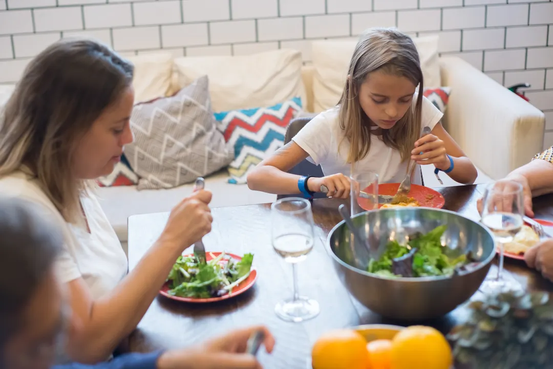 Eine Mutter und ihre Tochter essen gemeinsam Salat am Tisch.