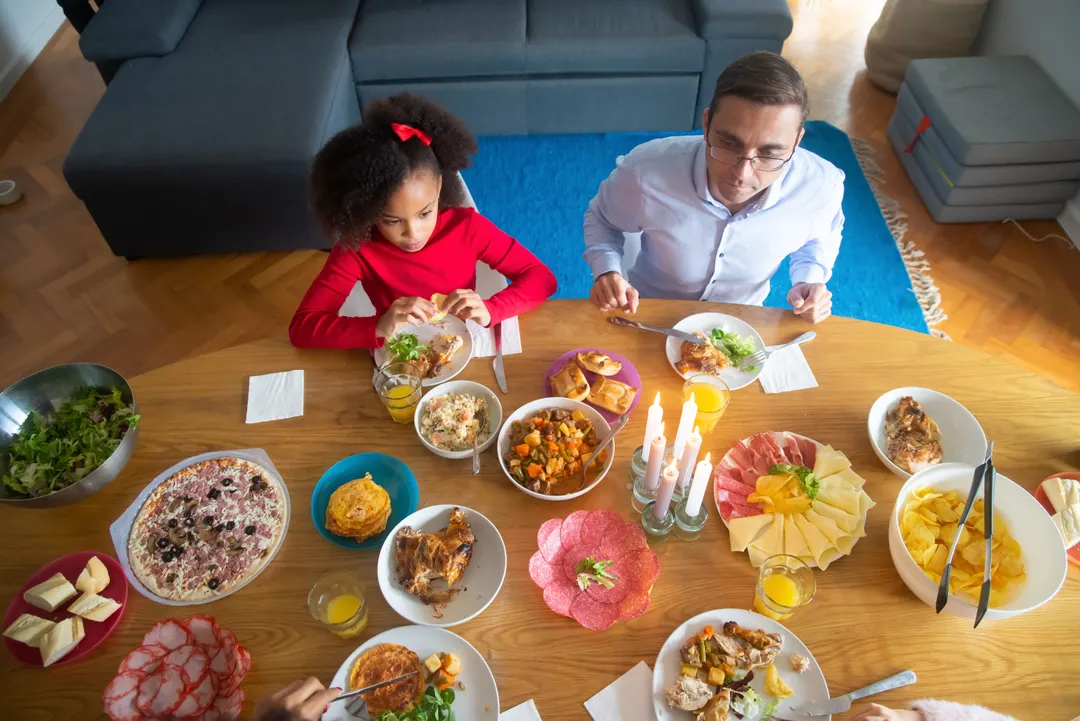Blick von oben auf einen gedeckten Tisch mit vielen kleinen Schüsseln, ein Vater und eine Tochter essen.