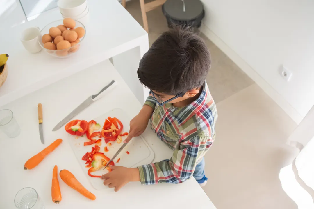 Ein Junge schneidet in einer hellen Küche Paprika und Möhren.