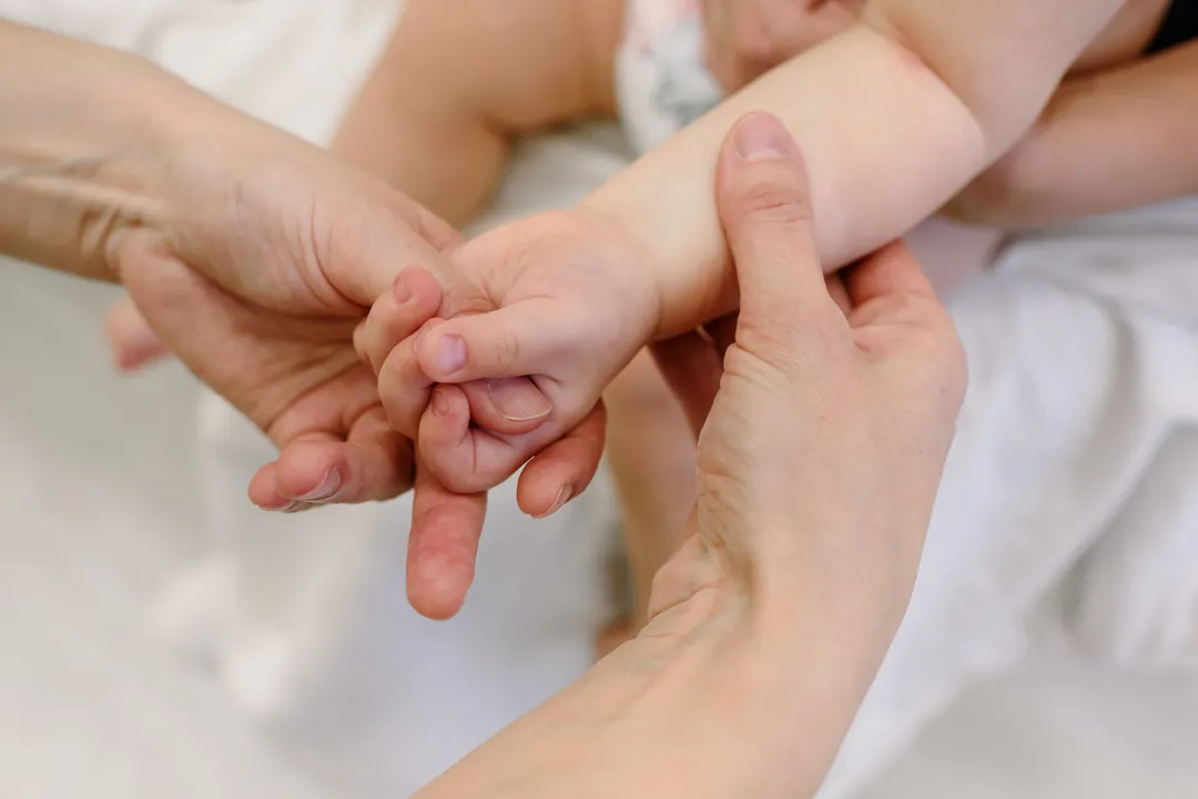 Eine Hand umschließt sanft den Arm eines Babys.