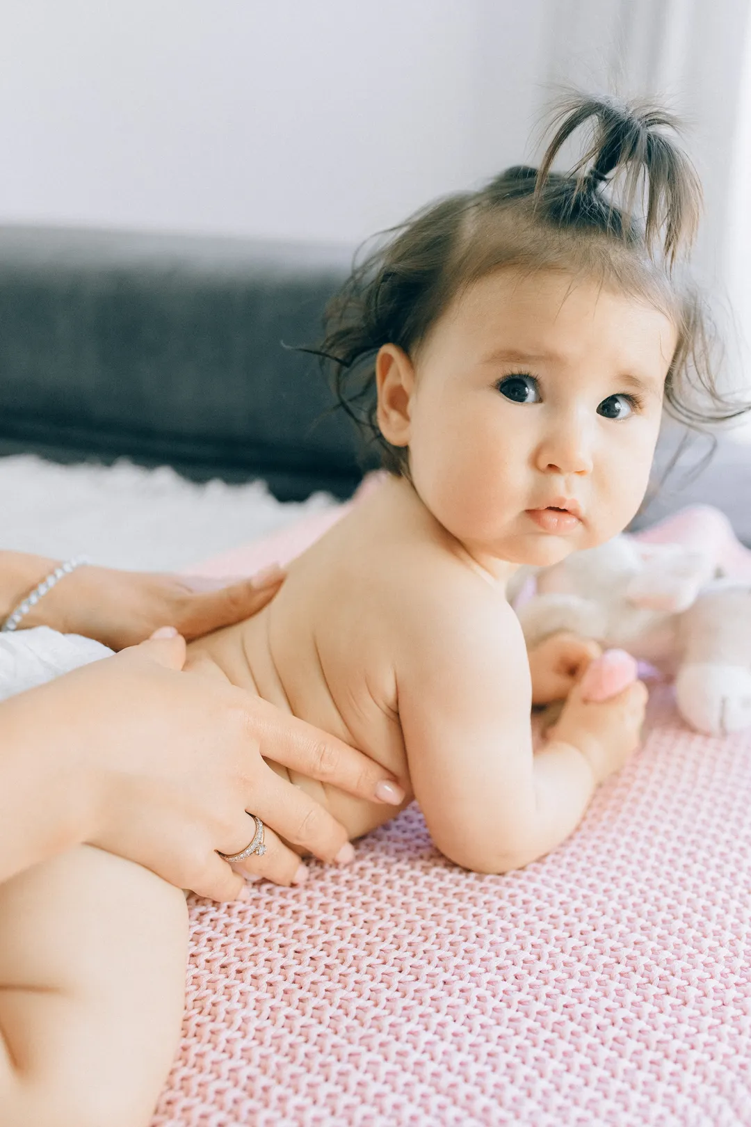 Ein Baby liegt auf dem Bauch und schaut neugierig auf, eine Hand liegt auf seinem Rücken.