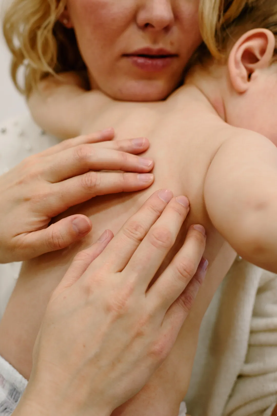 Eine Mutter streicht ihrem Baby über Brust und Schultern.