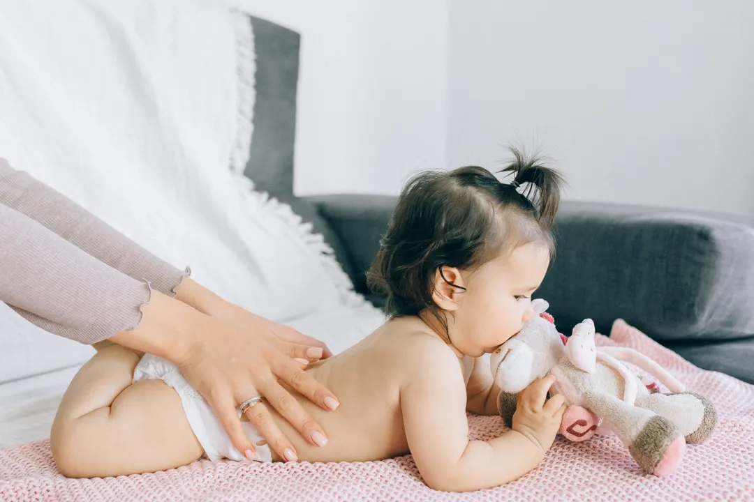 Ein Baby liegt auf dem Bauch, eine Hand streicht über seinen Rücken.